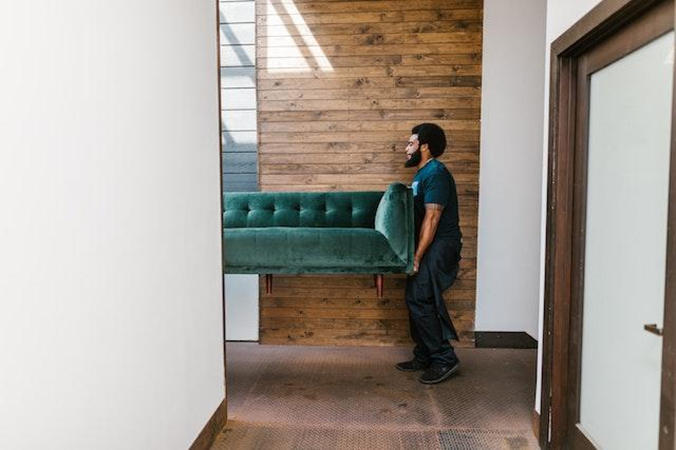 man in blue denim jeans carrying a green sofa